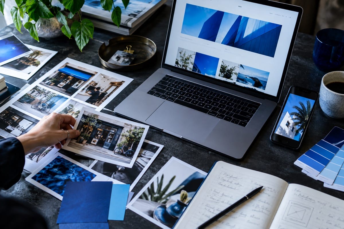 Illustrative creative workspace with campaign photographs, blue color samples, a laptop, and a phone